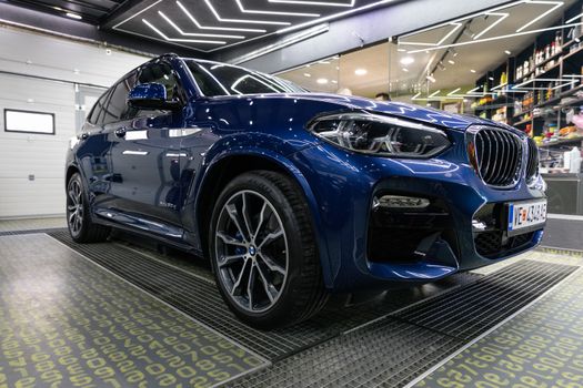 A sleek blue BMW X3 SUV showcased inside a contemporary garage setting.